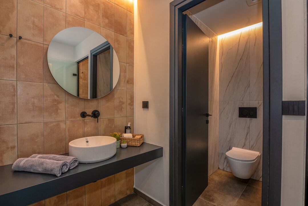 Contemporary bathroom with vessel sink, round mirror, terracotta tiles, and matte black fixtures at Nusa Gramvousa, Crete