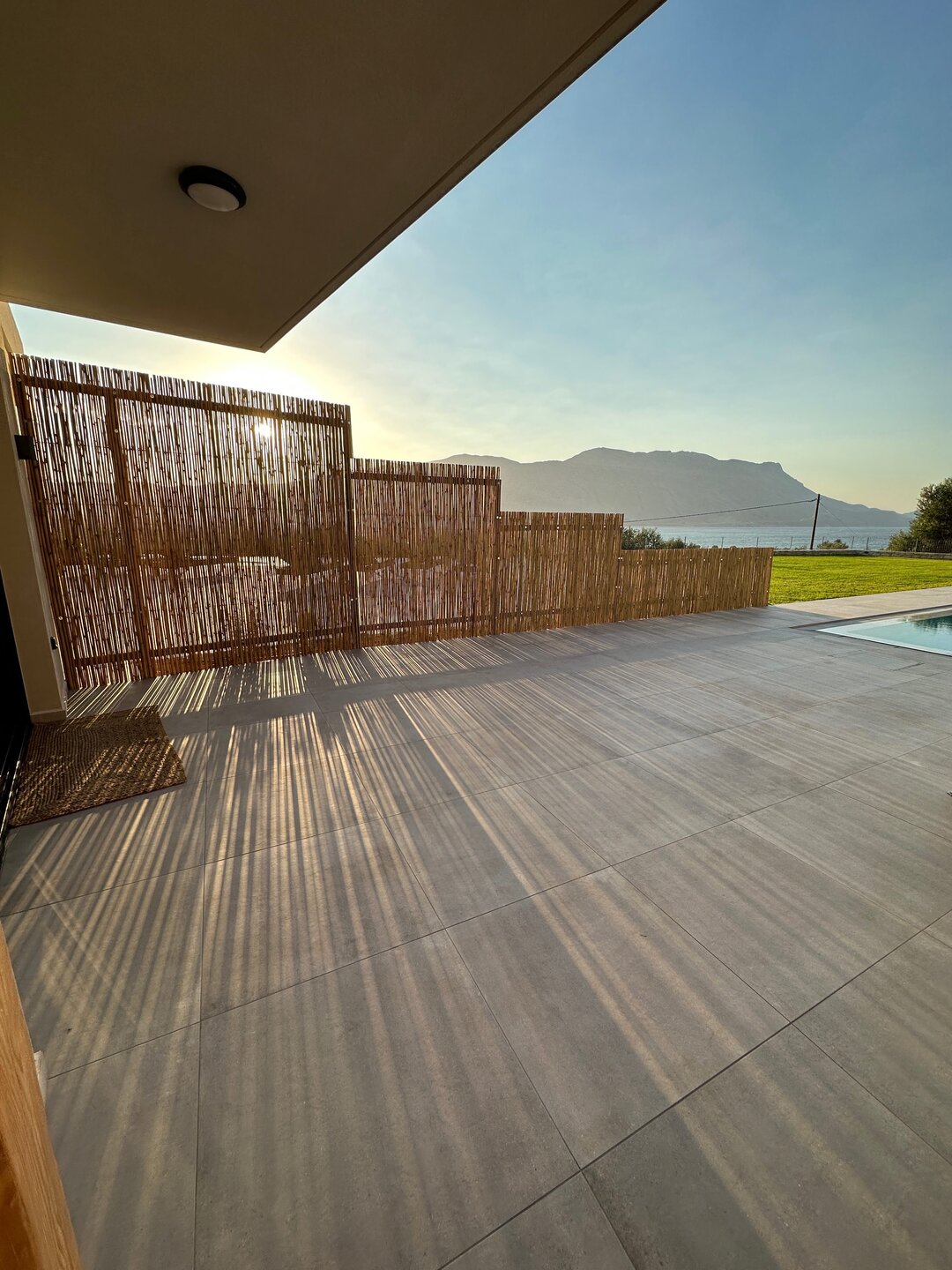 Stone patio with reed privacy screens casting sunset shadows beside the pool at Nusa Gramvousa, Crete